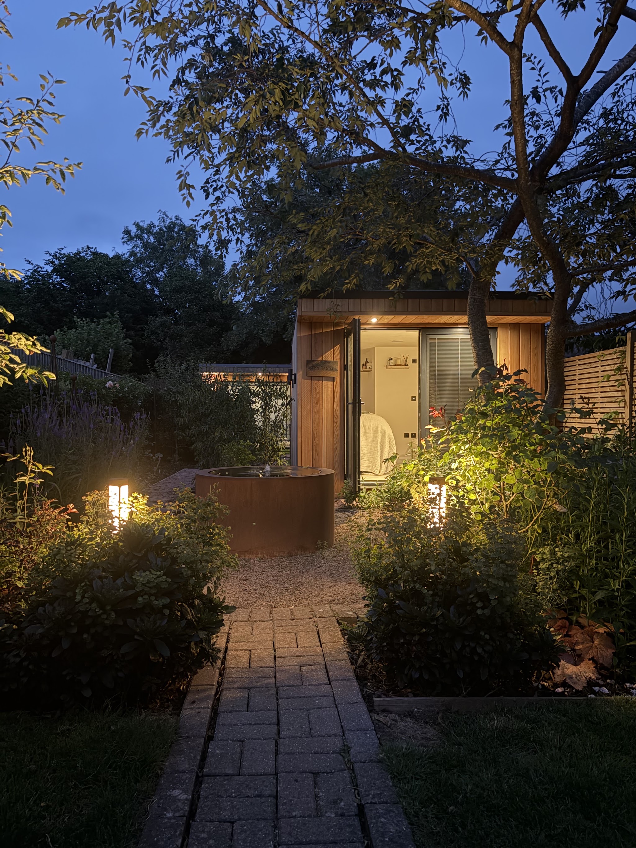 The lit brick path through the garden to The Retreat's timber studio at dusk