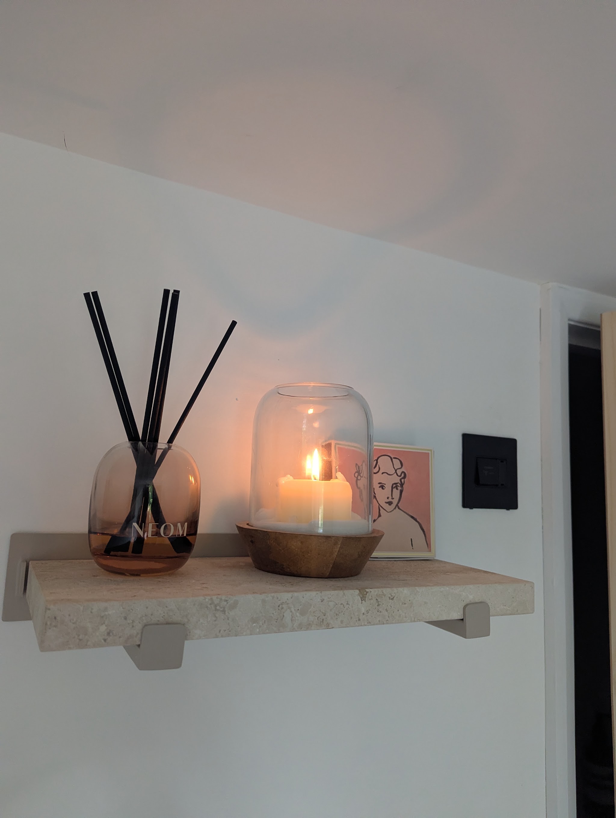 A reed diffuser and a lit candle on a stone shelf inside the studio