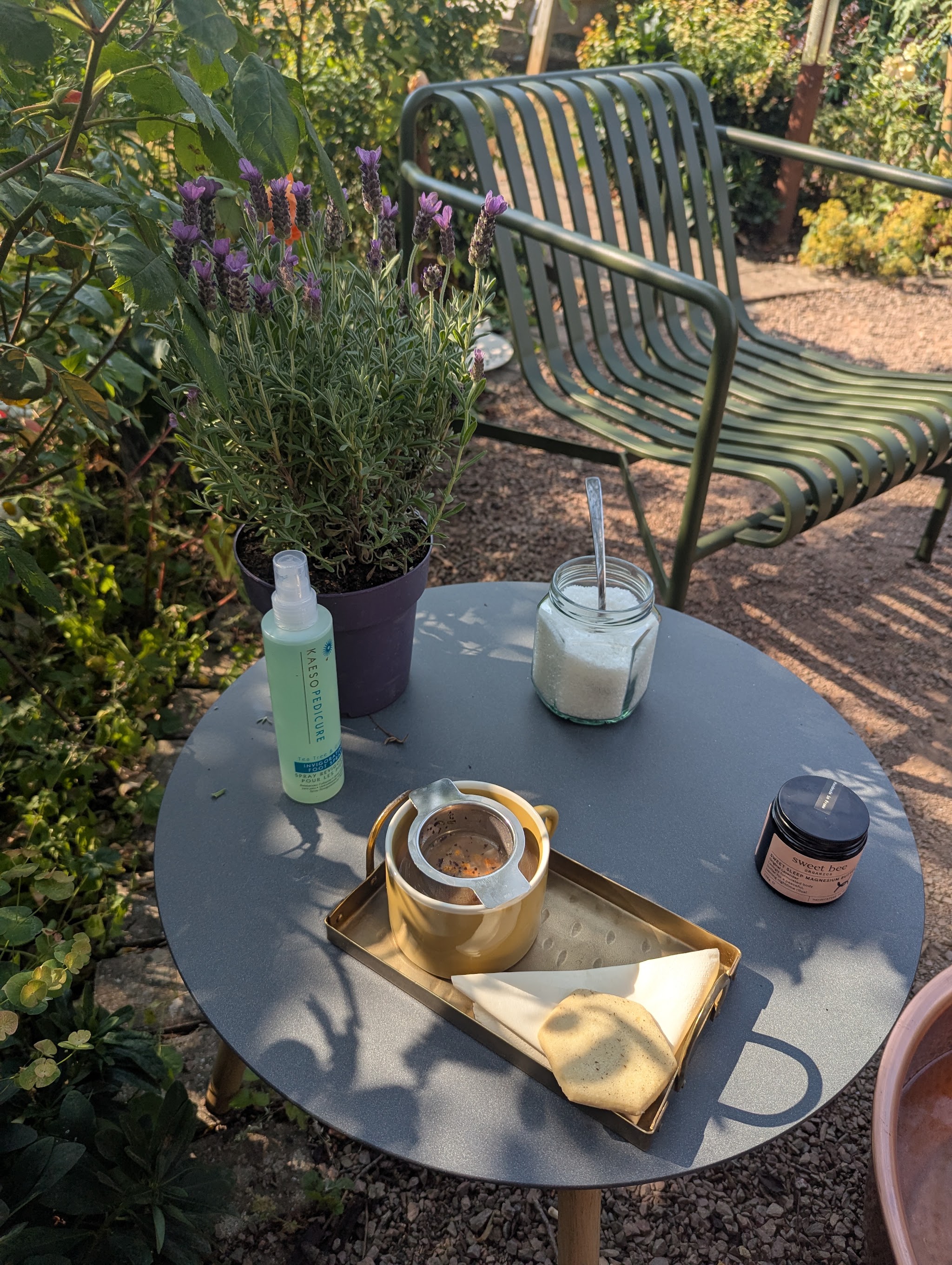 A garden table set with a tray, herbal tea and lavender beside a green chair