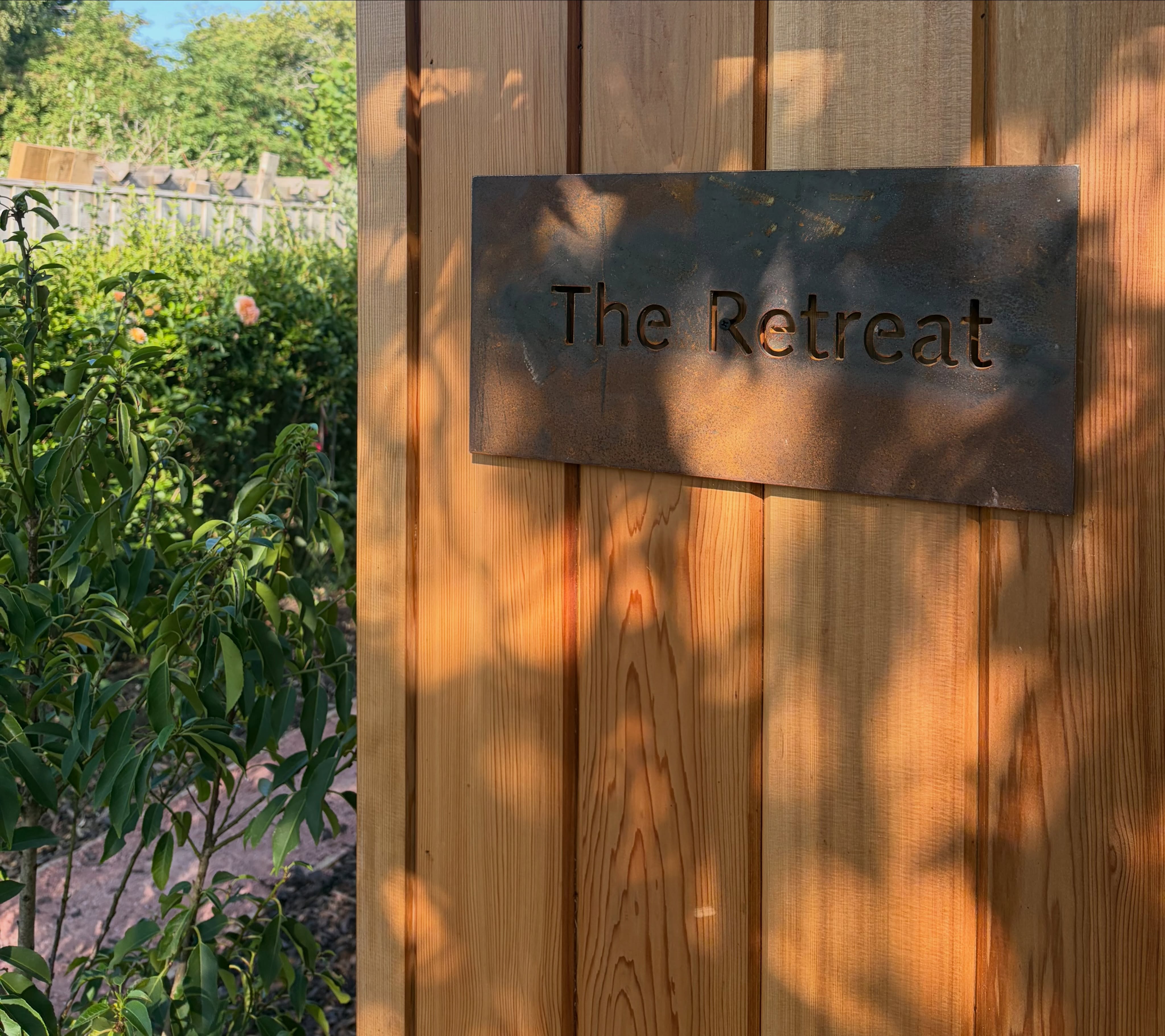 The corten steel The Retreat sign on the studio's timber cladding in evening sun